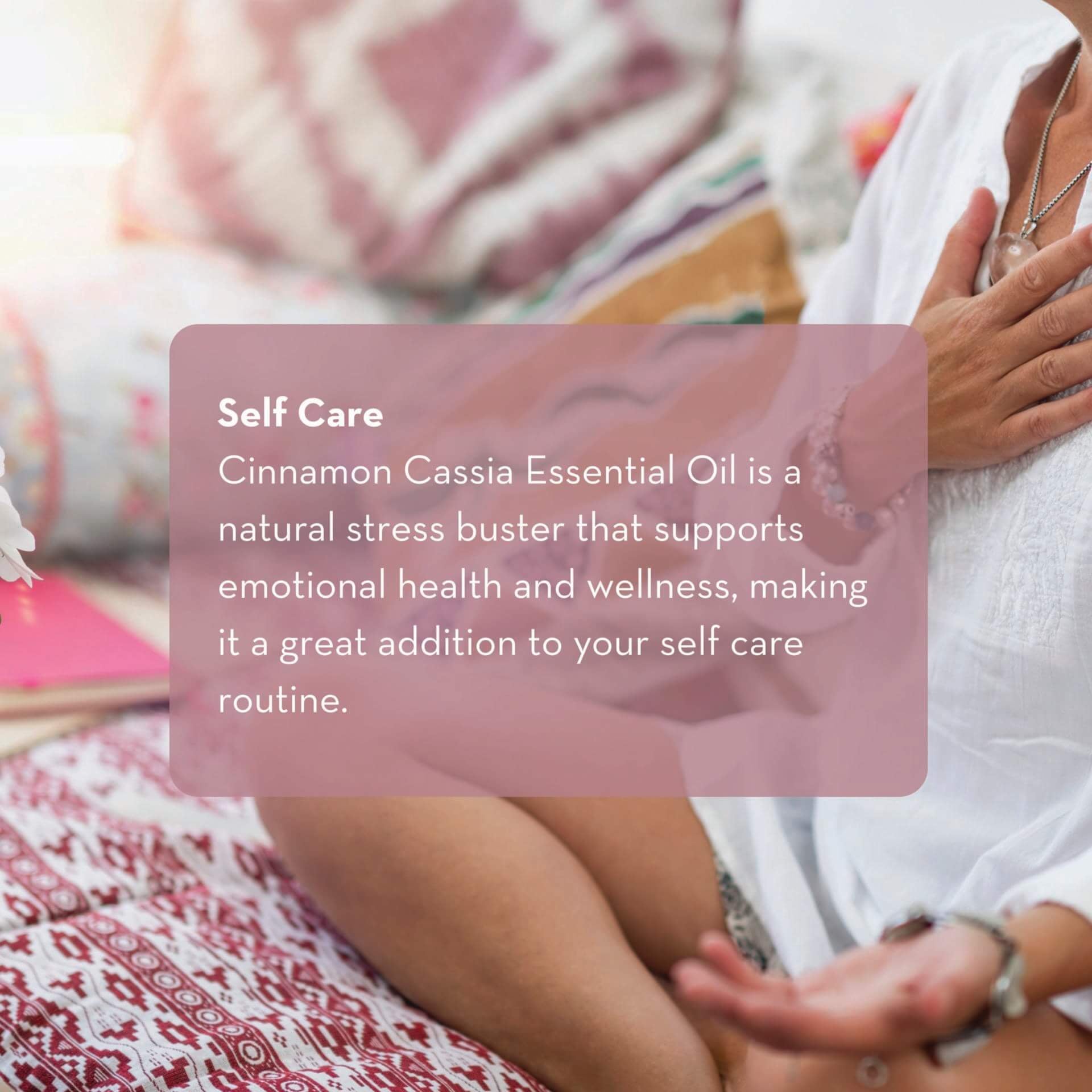 A person sits cross-legged on a patterned surface with a colorful pillow behind them, wearing a white outfit. A text block reads, "Self Care: Cinnamon Cassia Essential Oil, 10 ml is a natural stress buster that supports emotional health and wellness, making it a great addition to your self care routine.