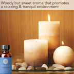 Bottles of Frankincense Essential Oil, 1 fl oz sit on smooth pebbles beside three lit candles. The background features warm, wood tones. Text above reads: "Woody but sweet aroma that promotes a relaxing & tranquil environment.