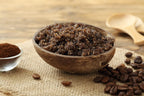 Wooden bowl filled with coffee scrub on a wooden surface with coffee beans around