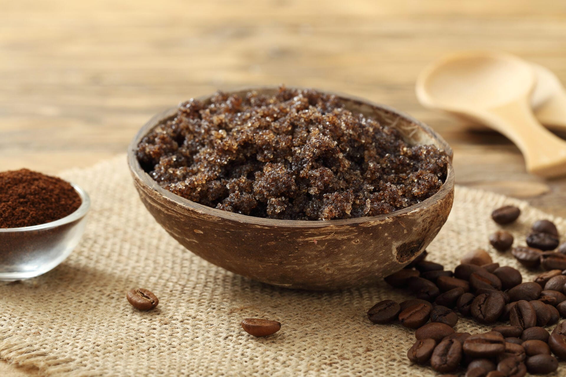 Wooden bowl filled with coffee scrub on a wooden surface with coffee beans around