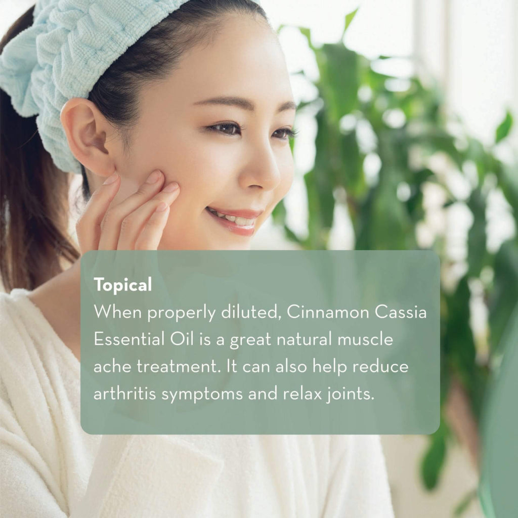 A smiling woman with a headband and a towel draped around her is gently touching her face. The background shows greenery. A green text box overlay reads: "Topical: When properly diluted, Cinnamon Cassia Essential Oil, 10 ml is a great natural muscle ache treatment. It can also help reduce arthritis symptoms and relax joints.
