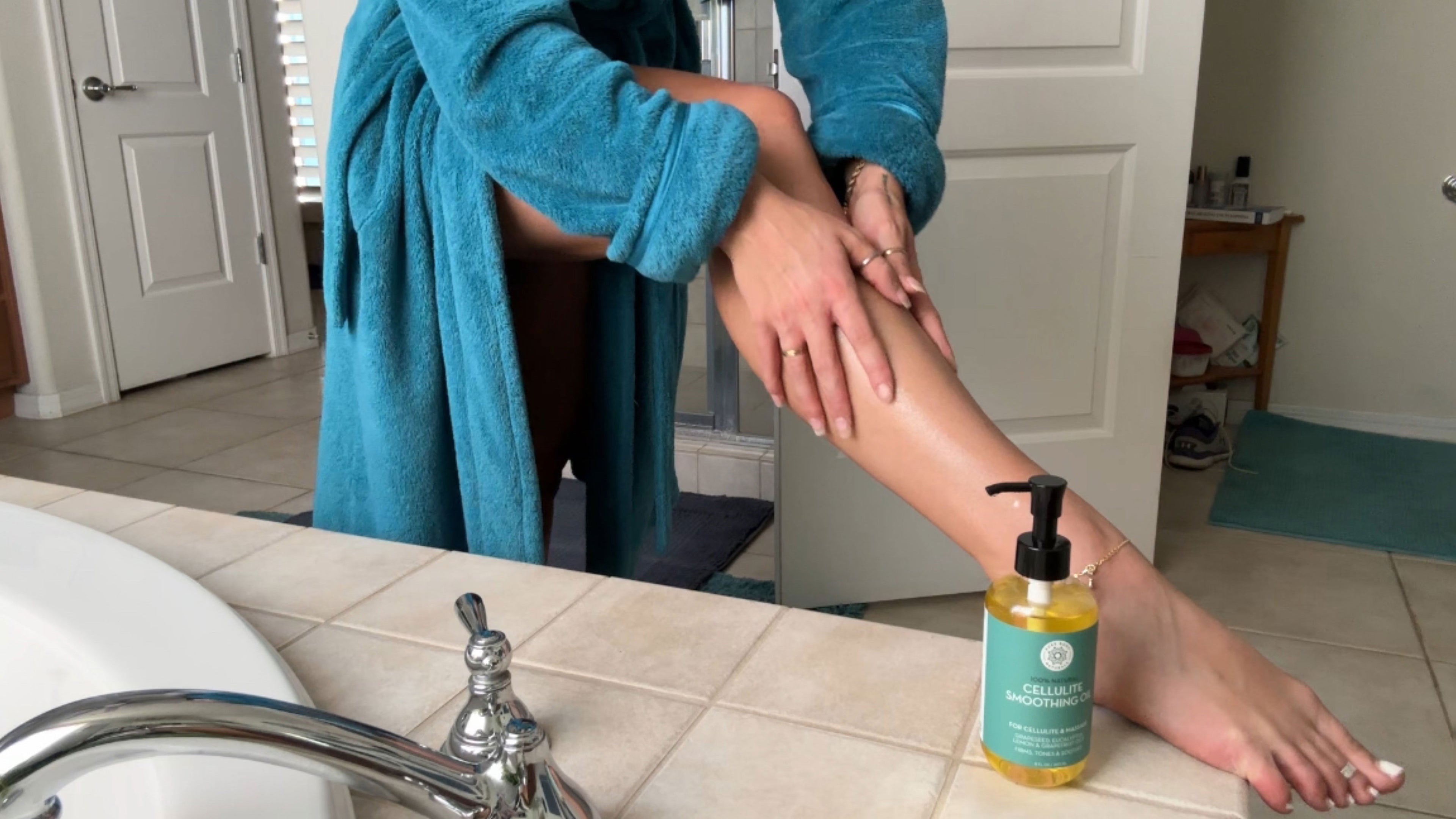 Person applying lotion to their leg with a bottle of lotion on the counter.